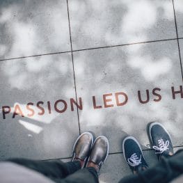 Two young people in sneakers standing above writing on the sidewalk that reads, "Passion led us here."