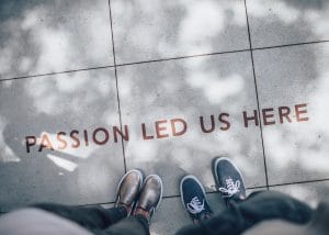 Two young people in sneakers standing above writing on the sidewalk that reads, "Passion led us here."